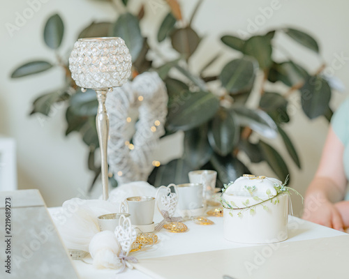 wedding rings displayed on a cake with greenery and candles in a celebratory indoor setting, close-up angle slightly elevated, white and green colors, fabric, glass, paper, metal materials.