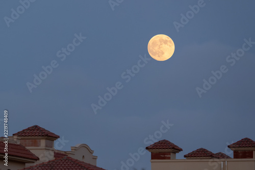 Fotografie Full moon glowing gold above rooftops at twilight