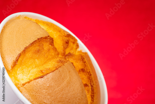 Fluffy baked souffle cake placed inside white cup against bright red background