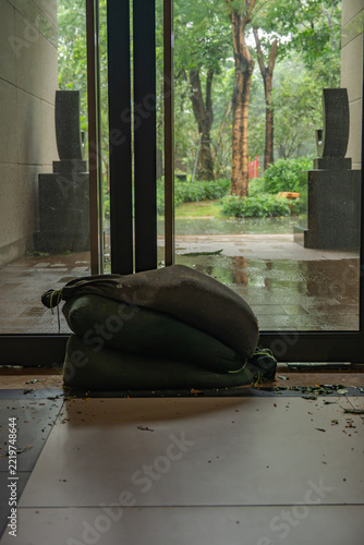 Sandbags stacked at glass entrance gate for flood prevention in rainy building lobby