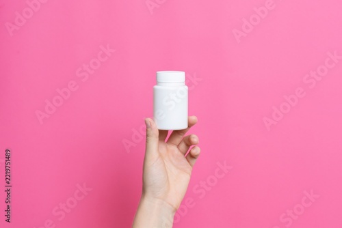 Hand holding white medicine pill bottle on pink background