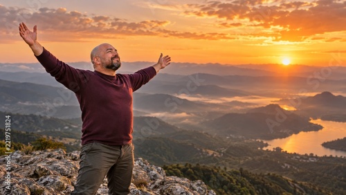 Man Standing with Raised Arms Above a Mountain Valley in Warm Sunset Light