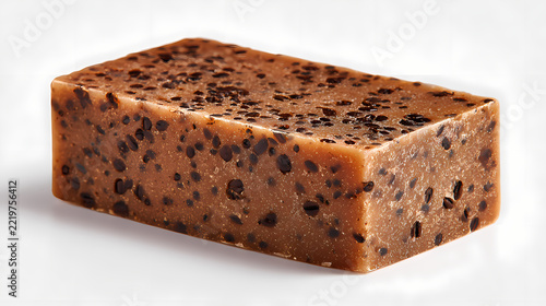 Exfoliating soap bar containing embedded coffee grounds rests on a bright transparent surface highlighting its textured surface.