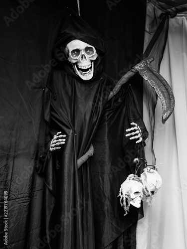 Obraz na plátně A hooded skeleton figure holds a scythe beside hanging skulls