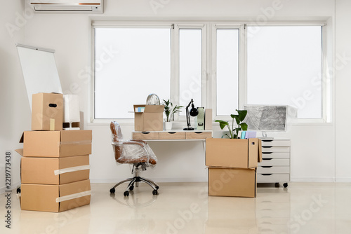 Corporate downsizing and office relocation, cardboard boxes and packed furniture in an empty workspace during business move or company restructuring
