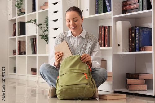Education and student life, young woman packing books into a backpack in a li...
