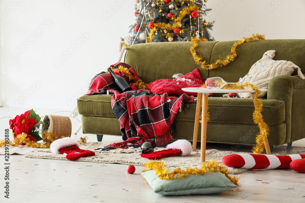 Fototapeta premium Post-party cleanup, messy living room after Christmas celebration with empty wine bottles and scattered holiday decorations on a green velvet sofa