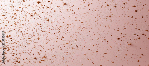 Brown bread crumbs scattered on a smooth light pink background