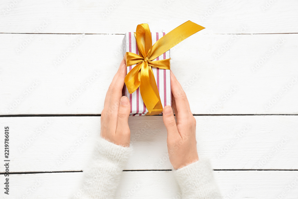 Fototapeta premium Gift giving and celebration, person holding a striped present with a gold ribbon on a white wooden table for holidays and special occasions