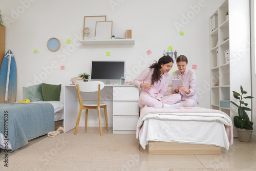 Digital childhood and remote learning, two teenage girls in pajamas using a t...