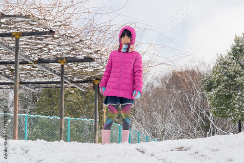 冬の雪が降る公園で楽しく雪遊びしてる小学生の女の子の姿
