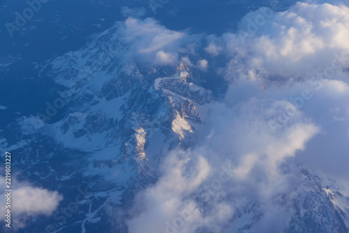 Aerial view of snow covered mountain peaks among clouds