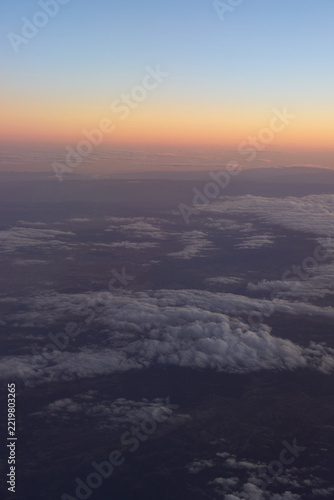 Orange sunset glow above clouds and dark land from airplane
