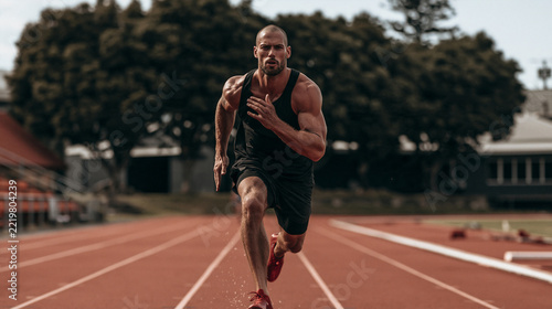 Speed and Power on the Track: A muscular male athlete sprints intensely on a red running track, his powerful physique on full display as he pushes his limits toward the finish line.