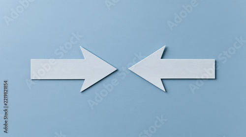 Two white arrows pointing in opposite directions on a light blue background. the arrows are made of paper and are positioned in a way that they are pointing towards the right side of the image.