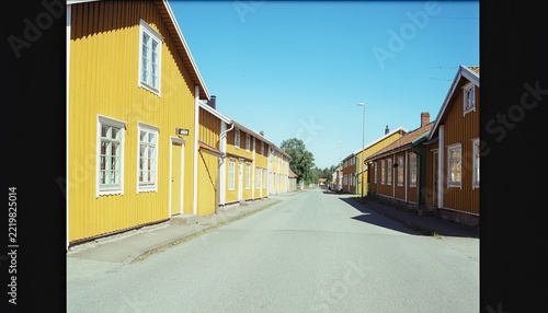 A picturesque street lined with vibrant yellow wooden houses under a clear blue sky.