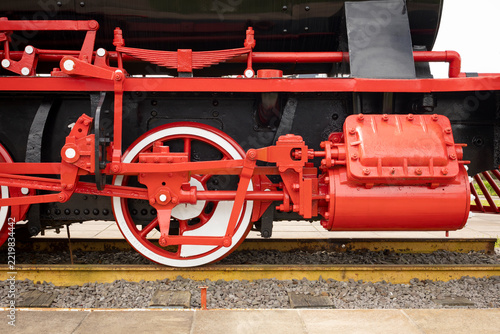 Side view of a historic steam locomotive wheel and red mechanism on tracks.