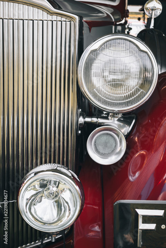 Restored vintage car front featuring chrome grille, headlights, polished details, and deep red bodywork.
