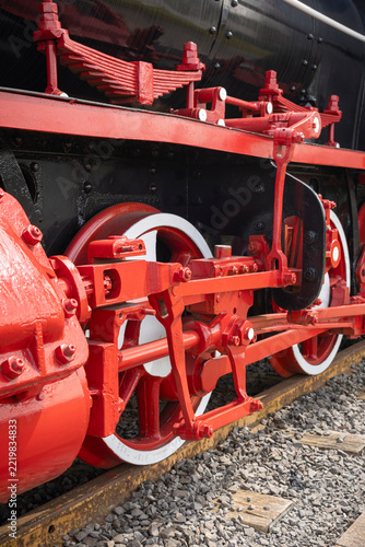 Close-up of red wheels, pistons, and mechanical parts of an old steam locomotive train on tracks.