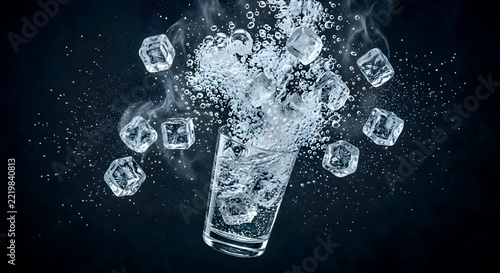 Ice cubes in a glass with water, water being poured into a glass with ice cubes floating, blue color is prominent in a cool and fresh drink