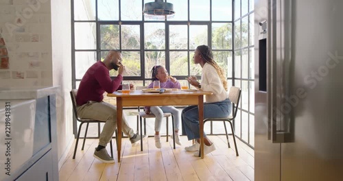African American family sitting at table sunlight drawing mom feeding child, dad lifting juice