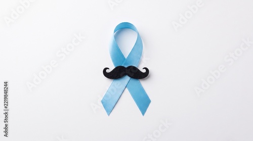 Light blue awareness ribbon with a black felt mustache on a clean white background, symbolizing men's health and prostate cancer awareness month