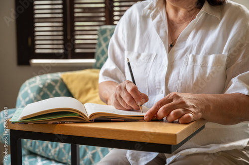 senior woman writing down her memories into a notebook, checking the budget etc copy space banner 