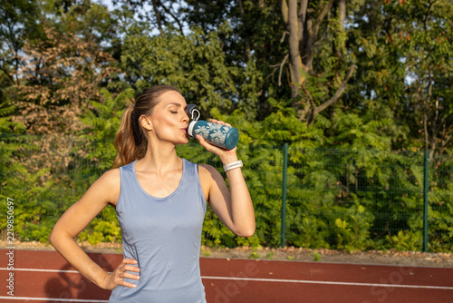 Obraz na plátně Athletic woman drinking water from a reusable bottle after a workout on an outdo