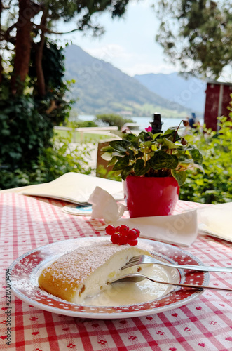 A slice of traditional Bavarian quark strudel dusted with powdered sugar, served with creamy sauce and red currants on a decorative red plate