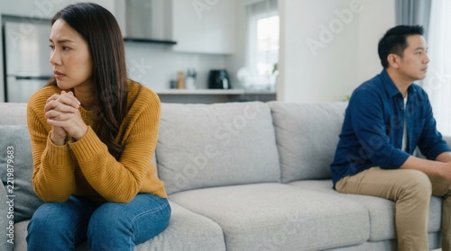 Asian husband and wife sitting back to back in the living room at home, showing a relationship problem and argument concept