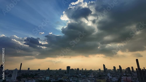 Time-lapse of Dark storm clouds surrounding bright sunlight over a densely developed cityscape in Thailand.