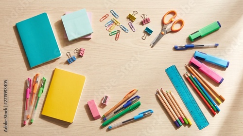 Assorted colorful stationery items arranged on a light wooden desk surface for school or office work
