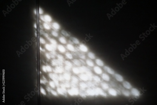 Abstraktes Motiv mit schwarz-weißem Licht-und Schattenspiel in Form eines weißem Lichtdreiecks mit Wellen- und Punktemuster vor schwarzem Schatten als Hintergrund