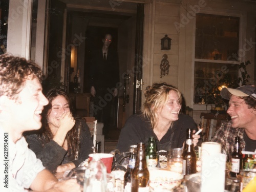 Unnoticed pale stranger watches a cheerful dinner party from the dark doorway