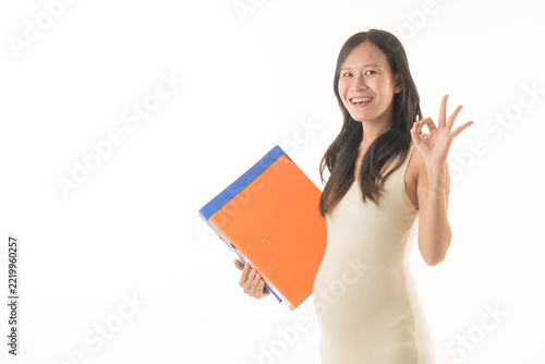 Obraz na plátně Smiling woman holding folder, making okay hand gesture, standing against white b