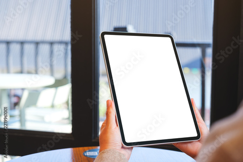 Mockup image of a woman holding digital tablet with blank white desktop screen in cafe