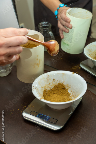 Person pouring henna powder into a bowl on a digital scale, preparing natural hair dye with herbal ingredients