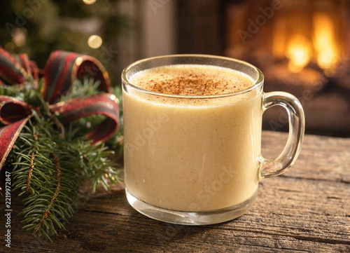 Glass mug of homemade traditional eggnog with cinnamon spice sitting on a rustic wooden table