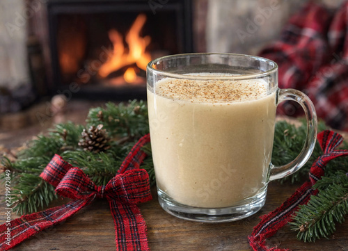 Glass mug of traditional eggnog holiday beverage sitting on wooden table with festive decorations