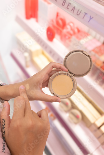 Woman's hands holding open compact powder foundation makeup with blurred cosmetic display background retail lighting
