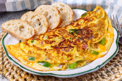 A breakfast Western omelet with ham, green bell pepper and onion with French bread slices