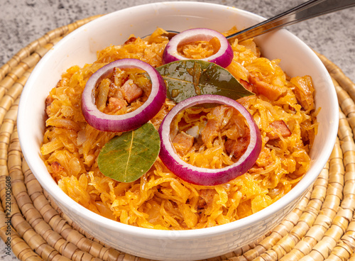 A dish of sauerkraut garnished with red onion slices and bay leaves on a woven mat