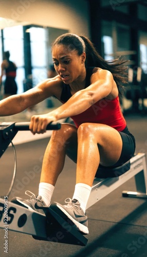 hyrox workout race concept. Woman exercising intensely on a rowing machine in a gym, showing focus and determination during a workout session.
