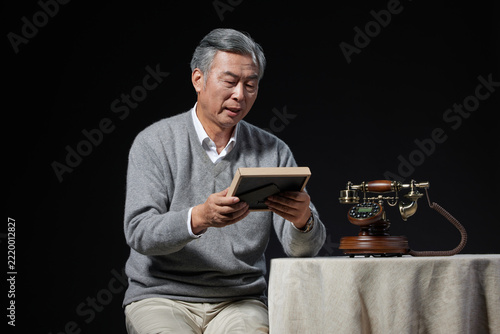 Fotografie Senior Asian Man Remembering with Framed Photo and Vintage Telephone