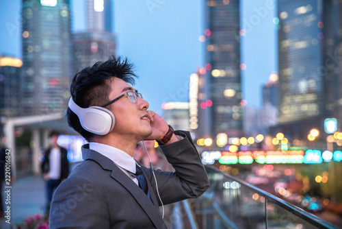 Photography Young businessman listening to music with headphones on a city balcony at dusk