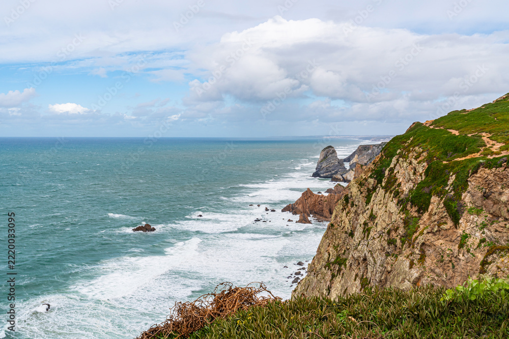 Fototapeta premium Cabo da Roca dramatic coastal cliff overlooking Atlantic Ocean in Portugal. Scenic westernmost point of Europe with rugged landscape, ocean waves and natural coastline.