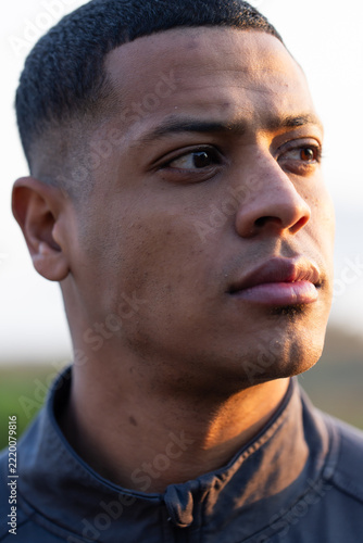 African American man looking right, wearing dark zip-up jacket with visible zipper pull outdoors