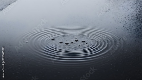 Raindrops creating ripples in a puddle on asphalt, rainy day