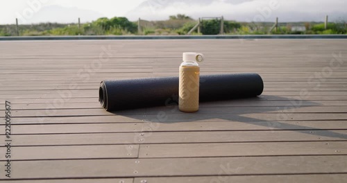 Camera is pulling back, tilting up, revealing rolled black mat, cream bottle on deck framing coast