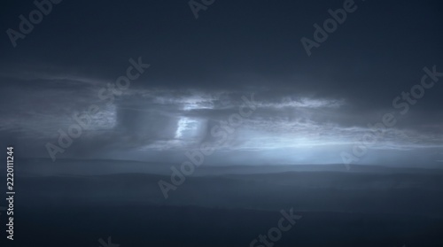 Moonlit pre-dawn storm clouds glowing softly in deep blue twilight, faint lunar light filtering through layered cloud banks